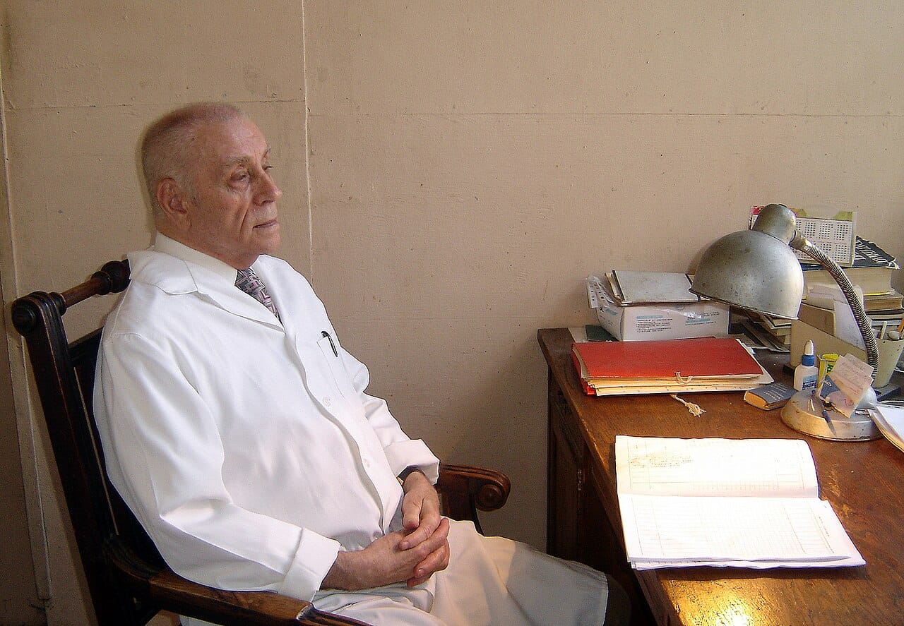 A researcher seated at a desk in a white coat, no equipment in reach.
