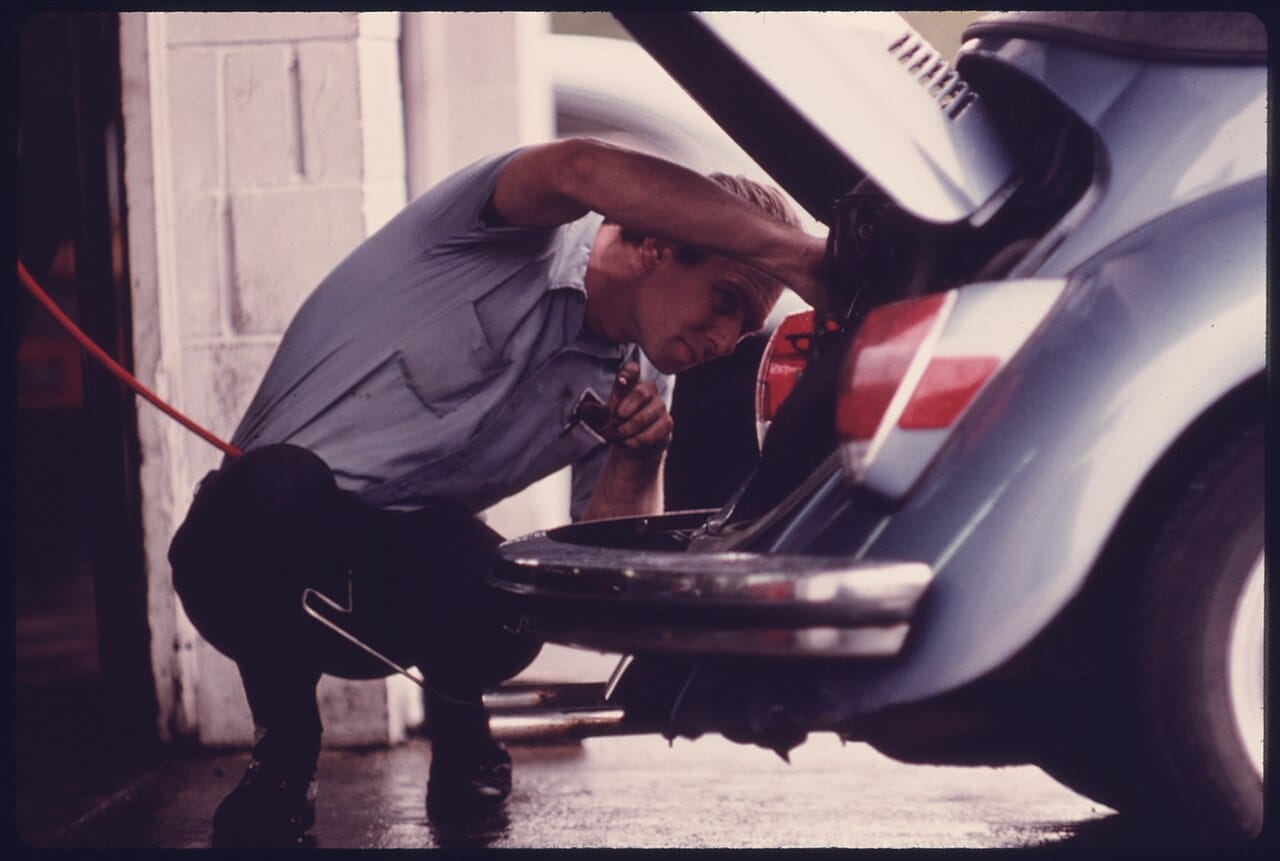 SERVICE STATION MECHANIC ADJUSTS THE ENGINE FOR A YOUNG WOMAN WHOSE VEHICLE HAD FAILED THE EMISSIONS TEST AT AN AUTO... - NARA - 557925