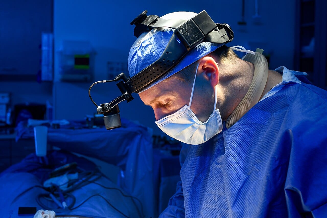 A surgeon wearing a headlight, scrubs and mask.