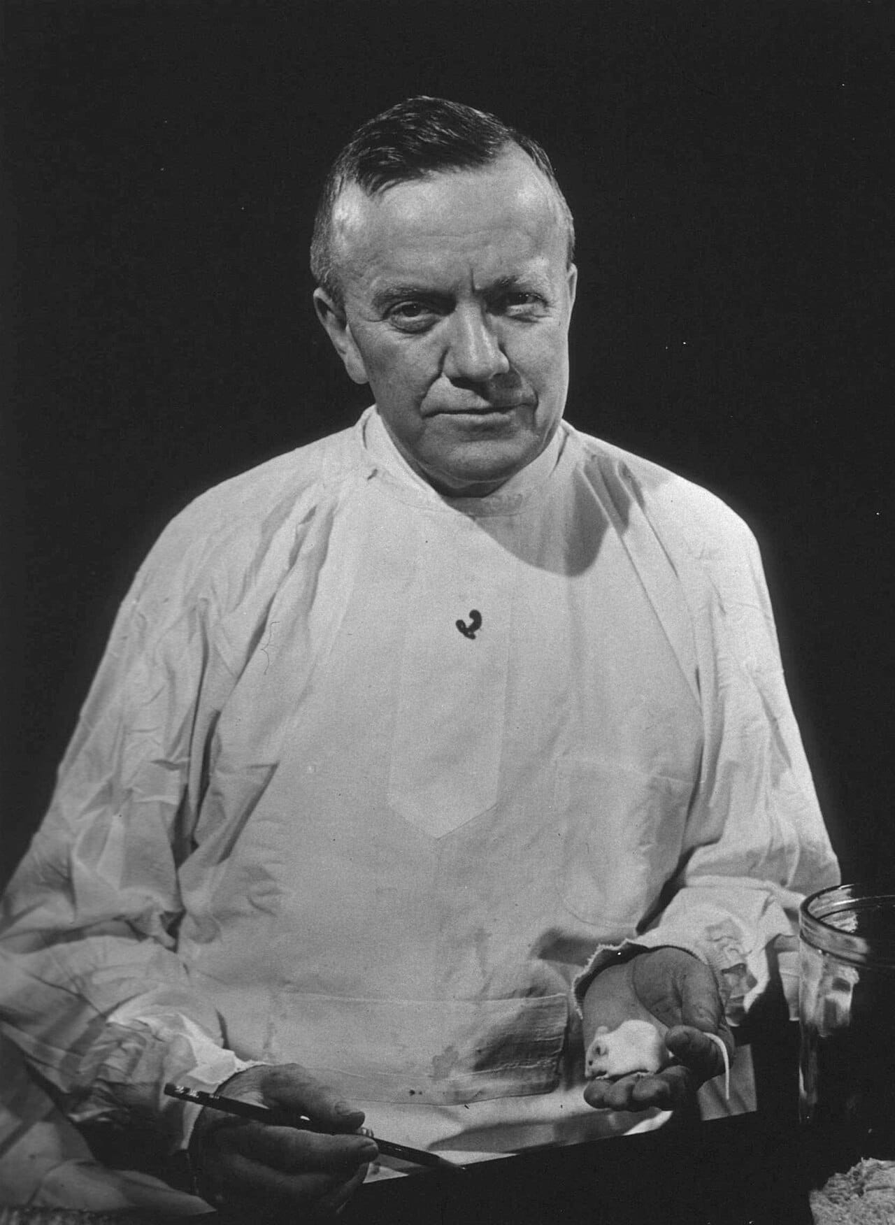 A bacteriologist photographed around 1950, in a white coat buttoned to the side.