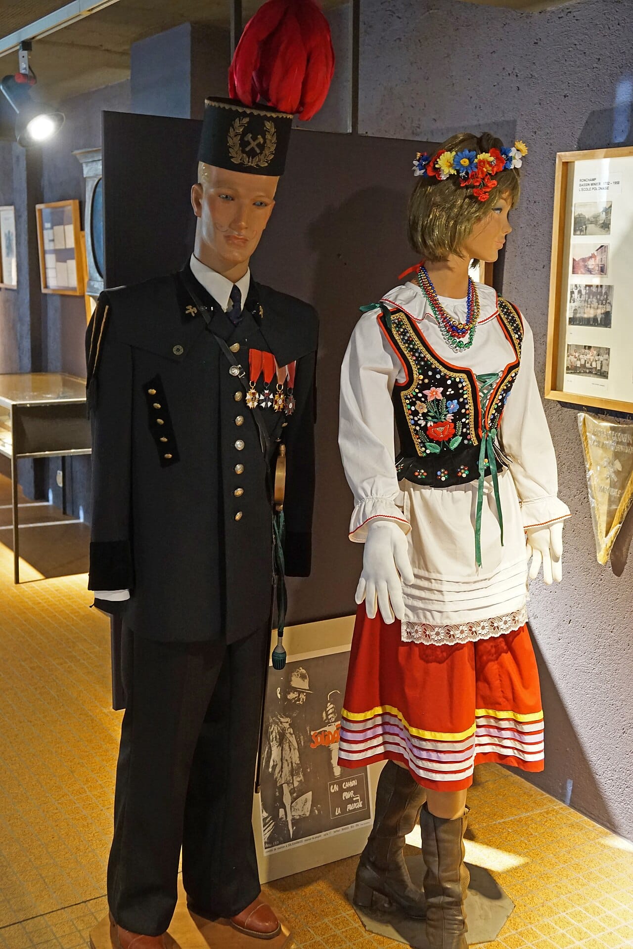 A miner's ceremonial coat on a museum figure, beside a woman's regional costume.