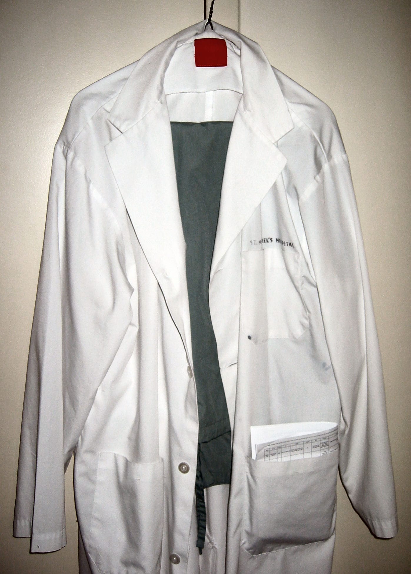 A lab coat hanging beside a set of scrubs.