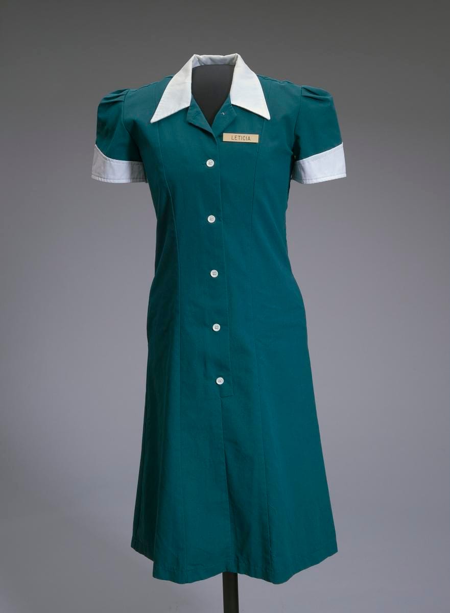 A teal waitress uniform, with the badge pinned above the pocket.