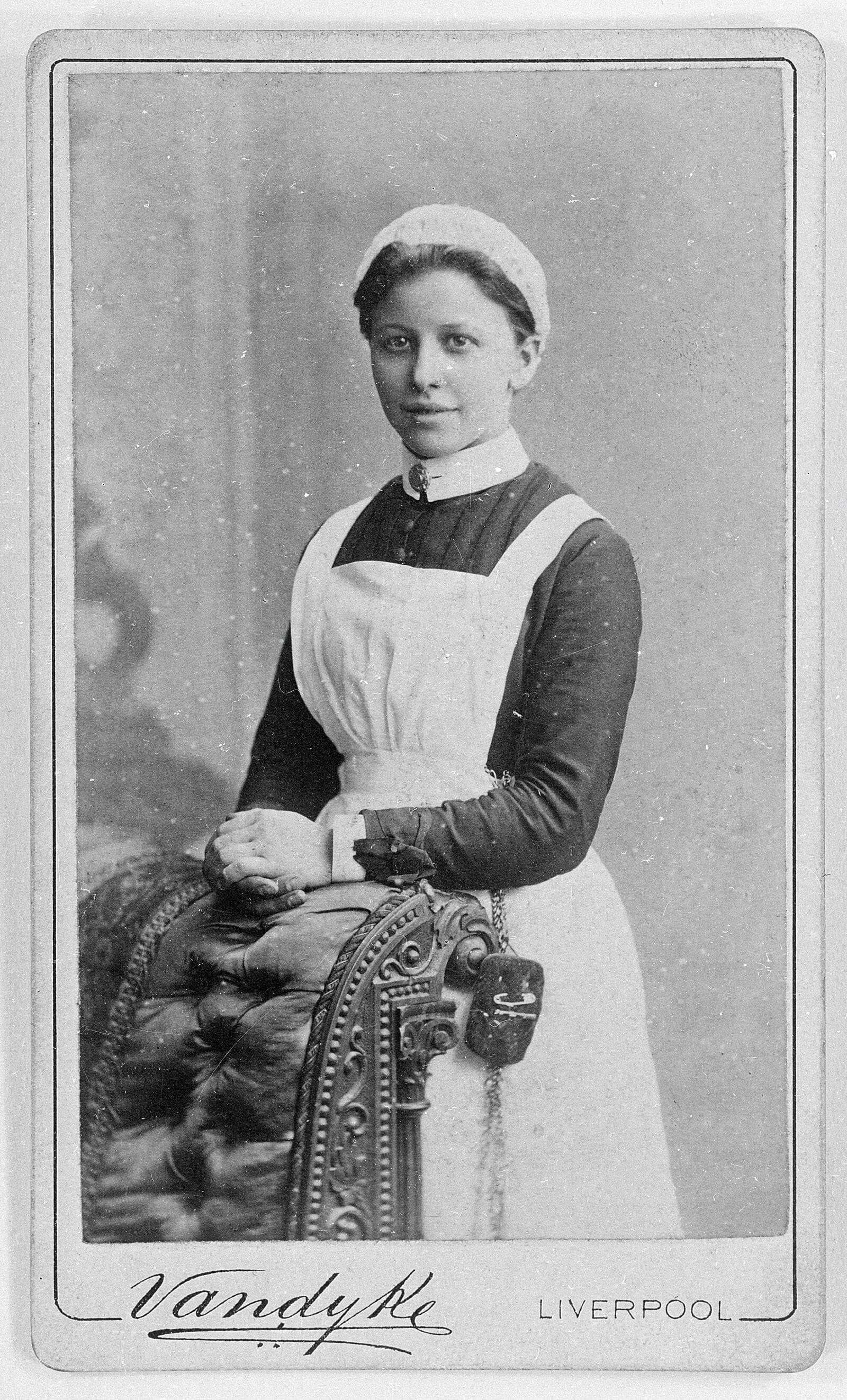 A nurse posed against ornate studio furniture, in uniform.