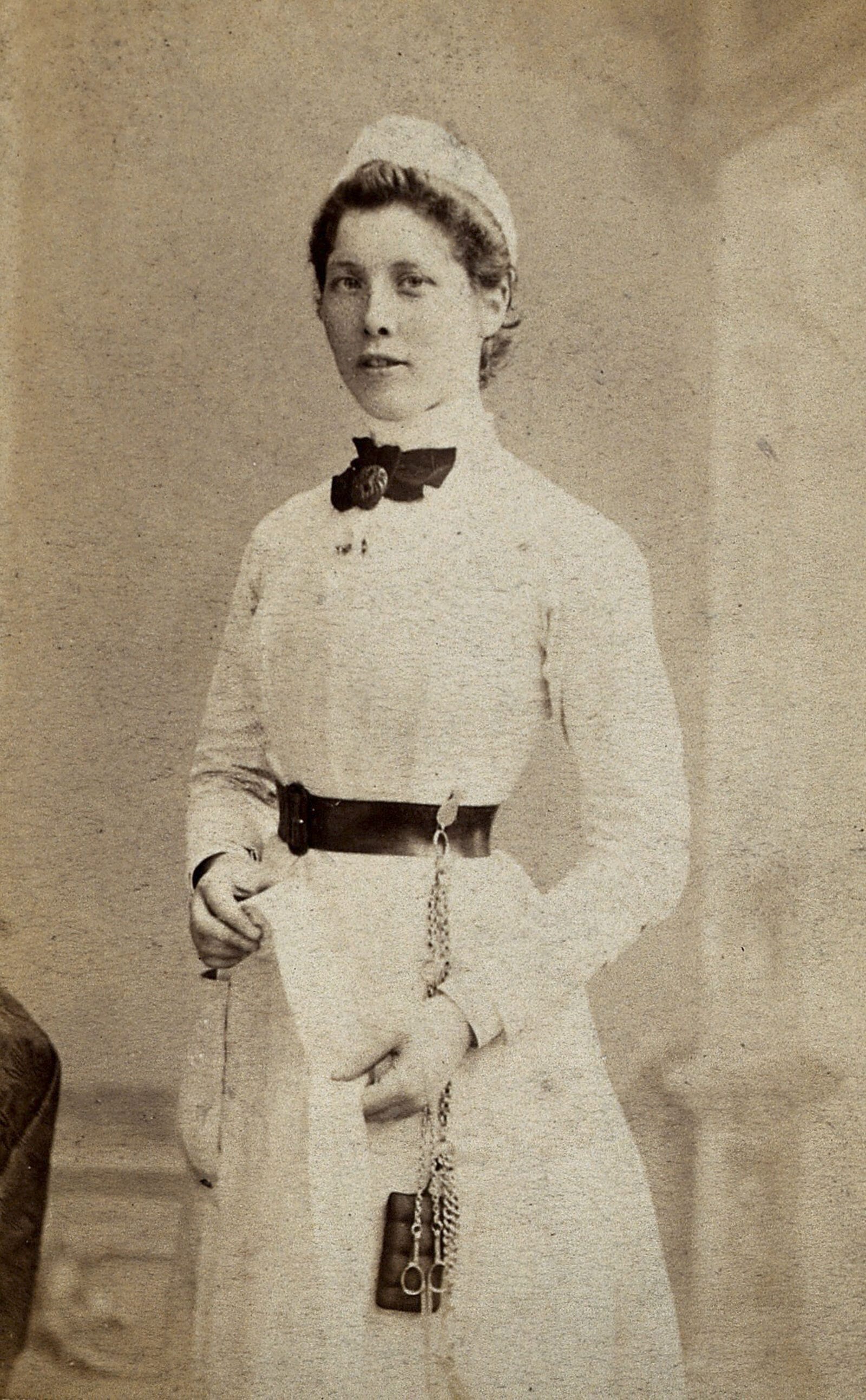 A nurse photographed in a studio, c. 1860–1880, standing for a full-length portrait in uniform.